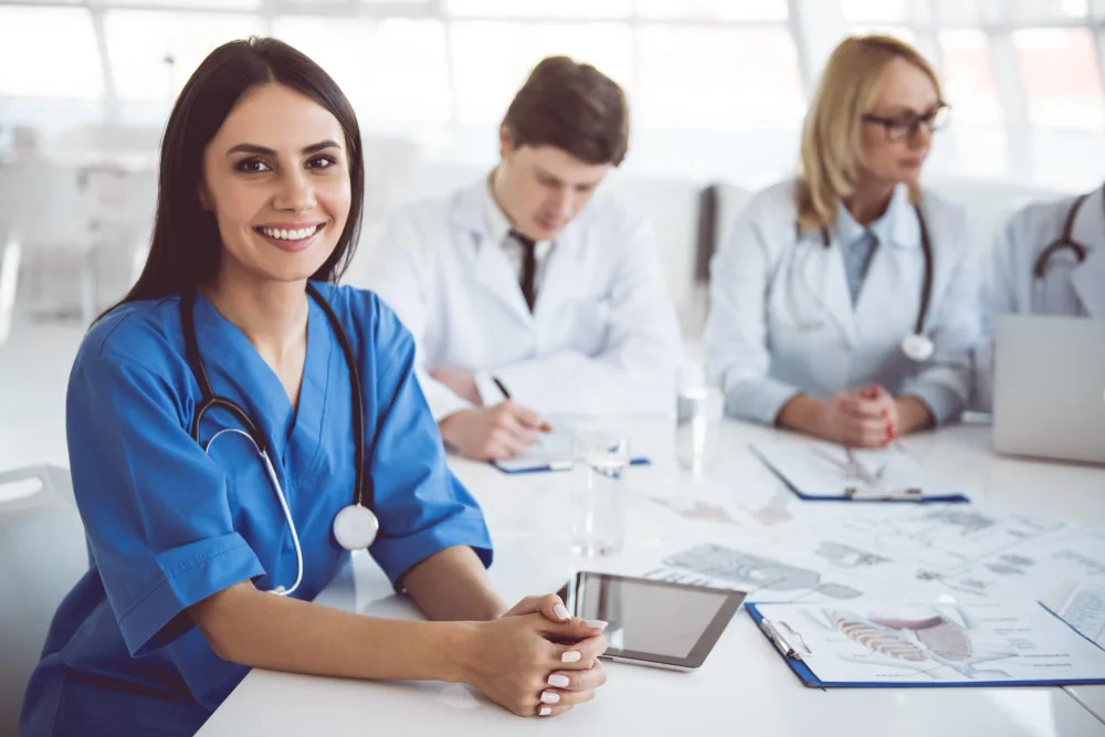 A female healthcare professional wearing a blue scrub and a stethoscope around her neck, smiling at the camera while holding a digital tablet, indicative of AI-enhanced healthcare content creation in the future