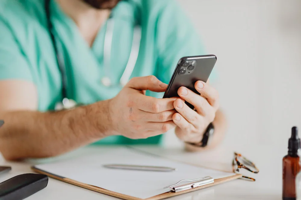 Close-up of a healthcare worker using a smartphone, possibly researching the latest digital marketing trends in the healthcare industry for 2024.