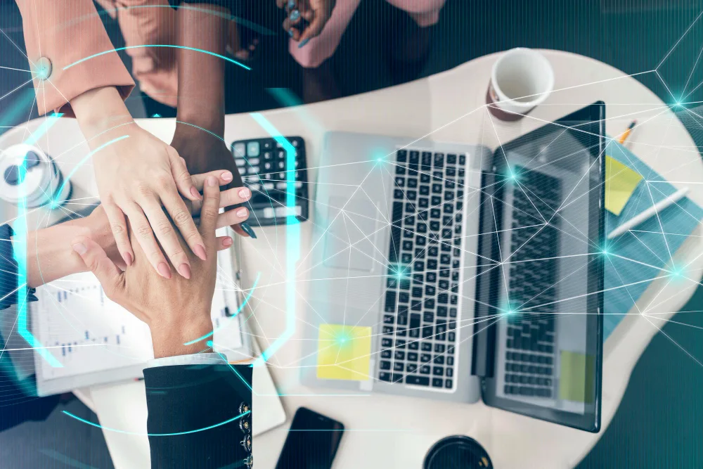 A group of hands coming together over a high-tech workspace, symbolizing teamwork in maintaining AI-human balance in the workplace.