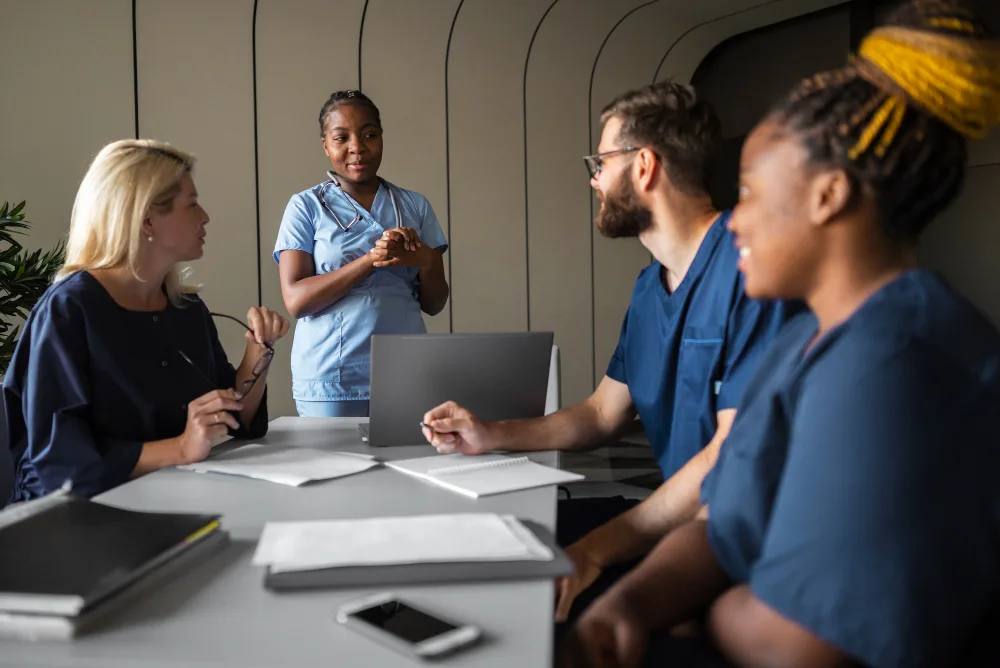 Healthcare staff engaged in a discussion around a laptop, representing the collaboration between AI tools and human expertise in medical strategies.